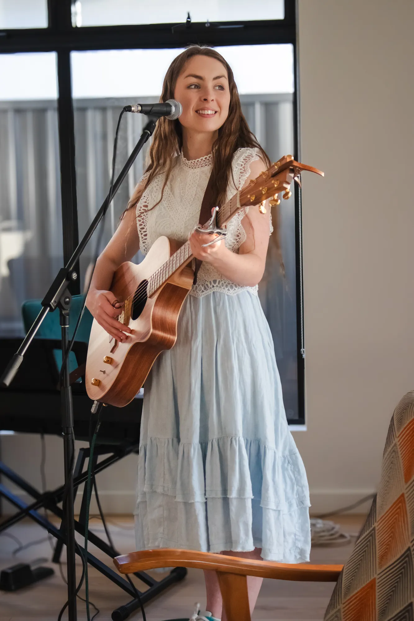 Solly Fern at the microphone with her acoustic guitar, smiling out at the room