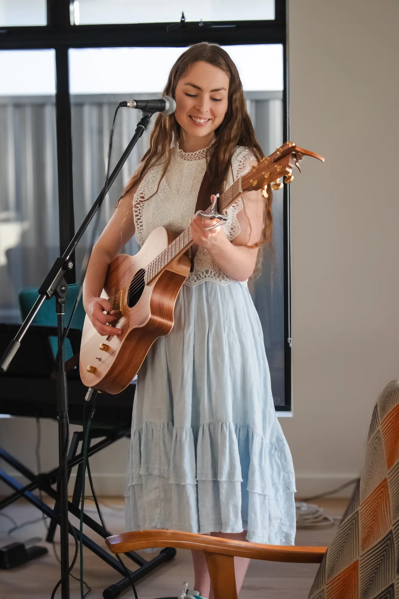 Solly Fern smiling as she sings and plays acoustic guitar in a light blue dress