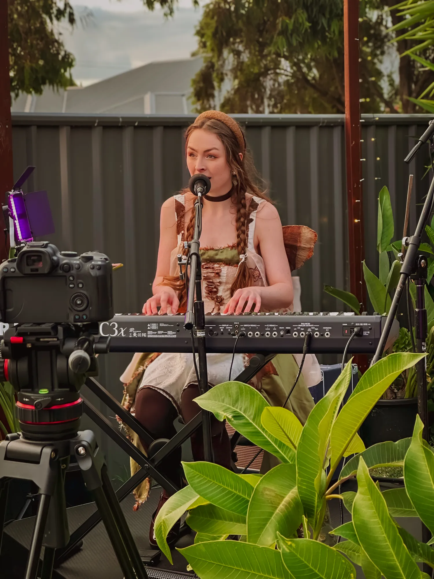 Solly Fern singing at a keyboard outdoors in a courtyard among potted plants