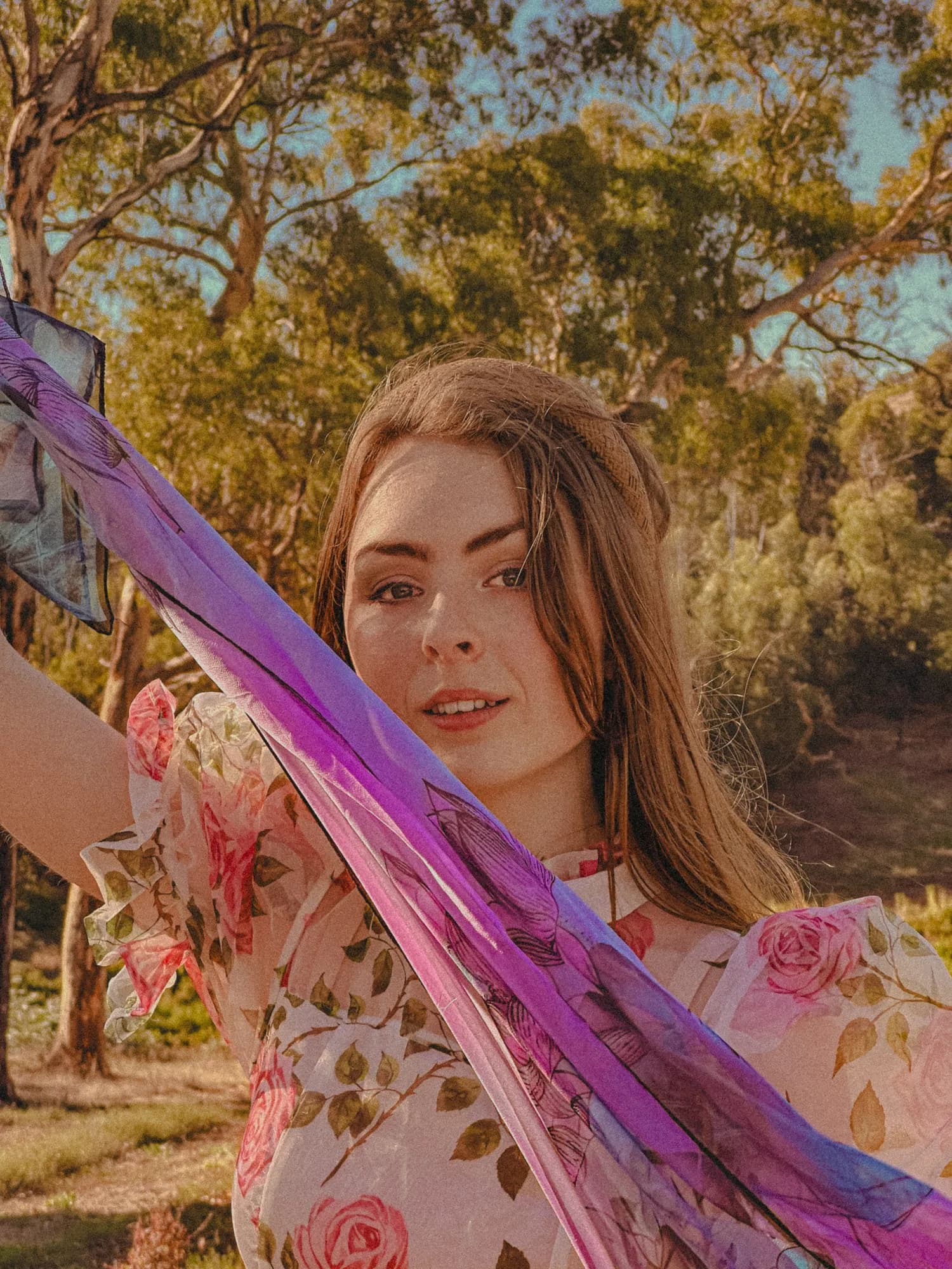 Solly Fern in a rose print dress among gum trees, holding a violet scarf