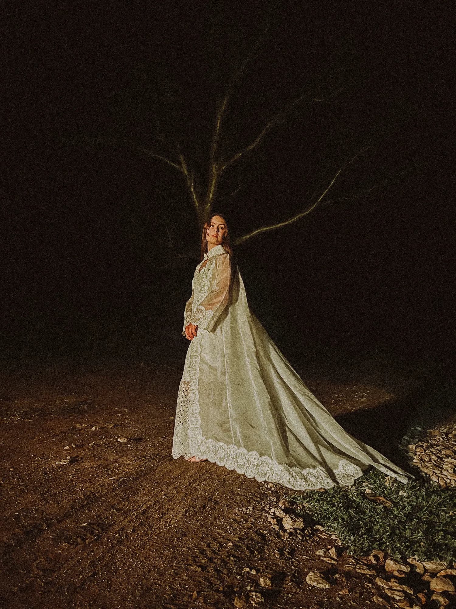 Solly Fern in a long lace gown beneath bare branches at night