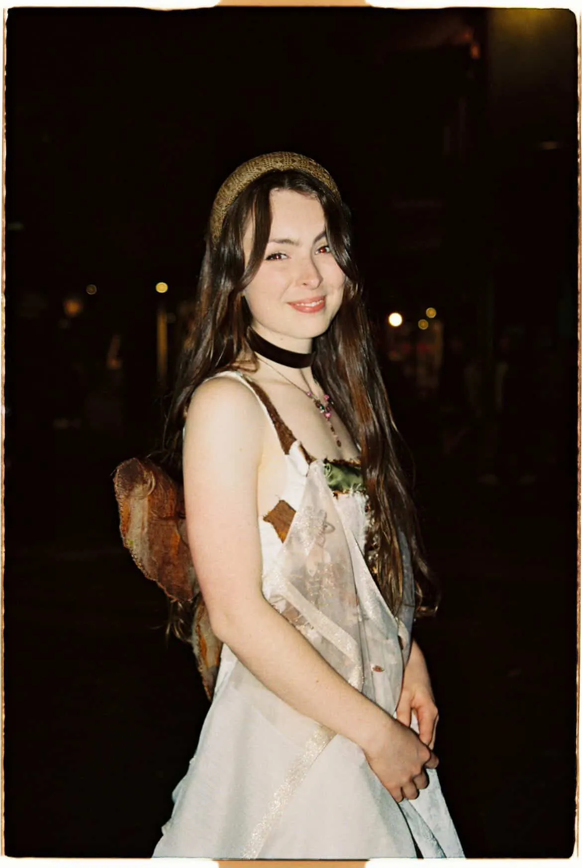 A film photo of Solly Fern smiling in a white slip dress and a velvet choker