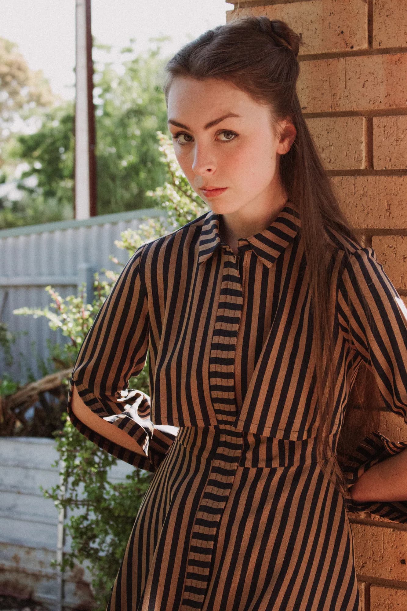 Solly Fern in a striped dress, leaning against a brick wall
